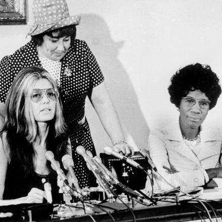 Trois femmes sont assises à une table, une a des microphones devant elle, suggérant qu'il s'agit d'une conférence de presse