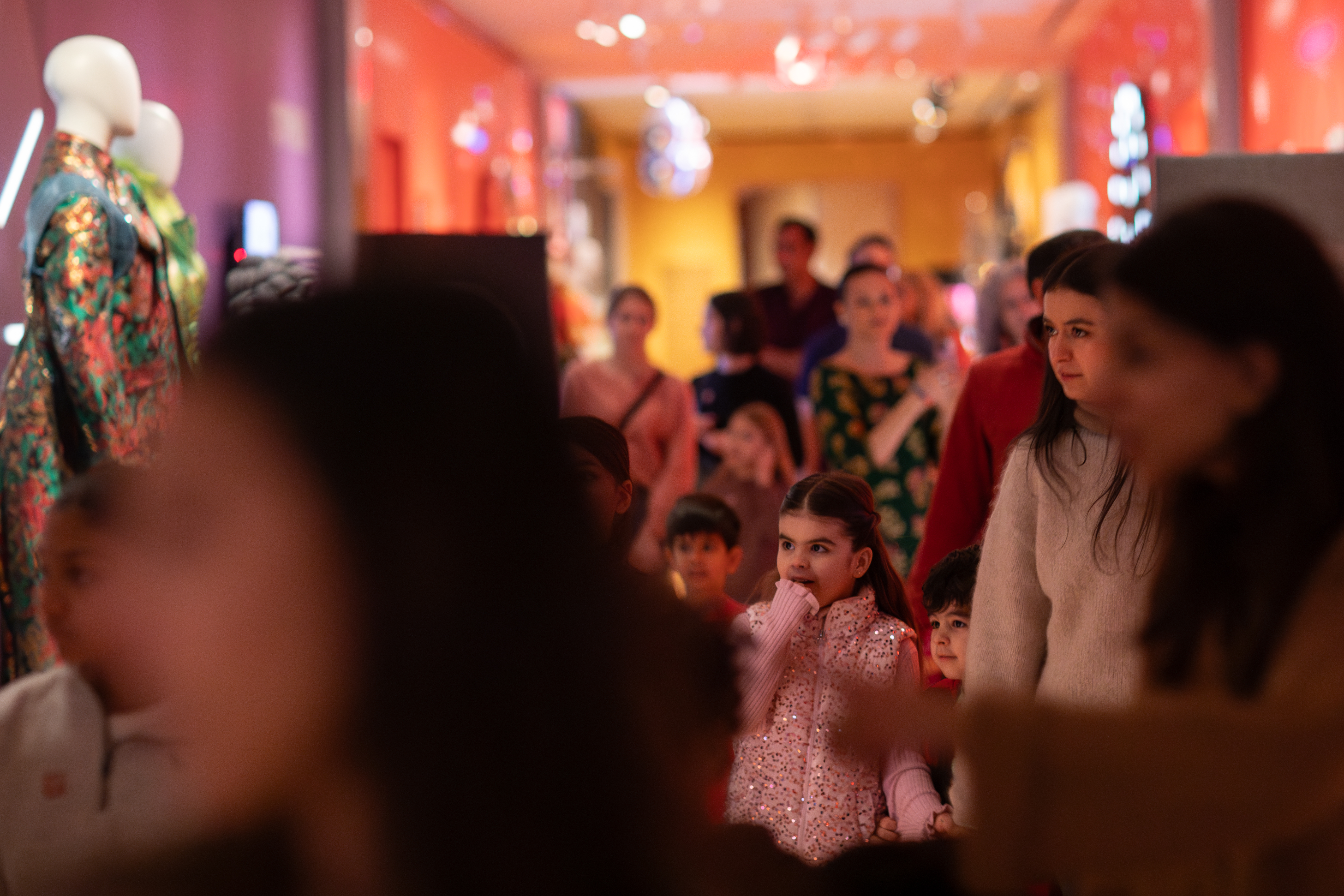 An image focused on a little girl looking mesmerized in a crowd of people walking down a colorful hallway