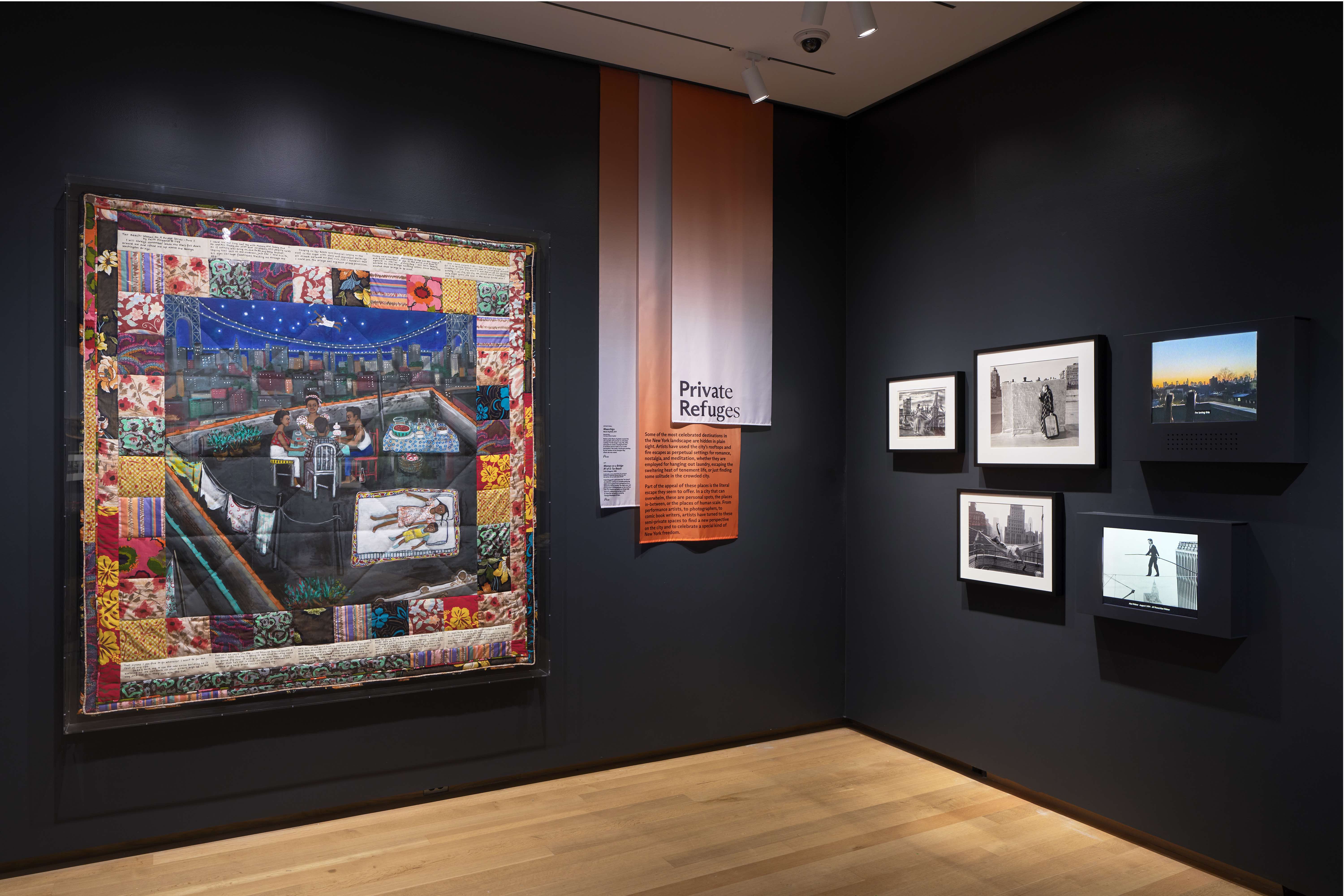 Uma colcha e imagens estão penduradas na parede de uma galeria.