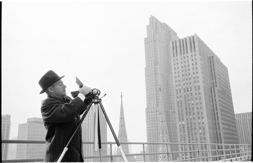 供以人员调整他的在一个三脚架的照相机有纽约地平线的在背景中。