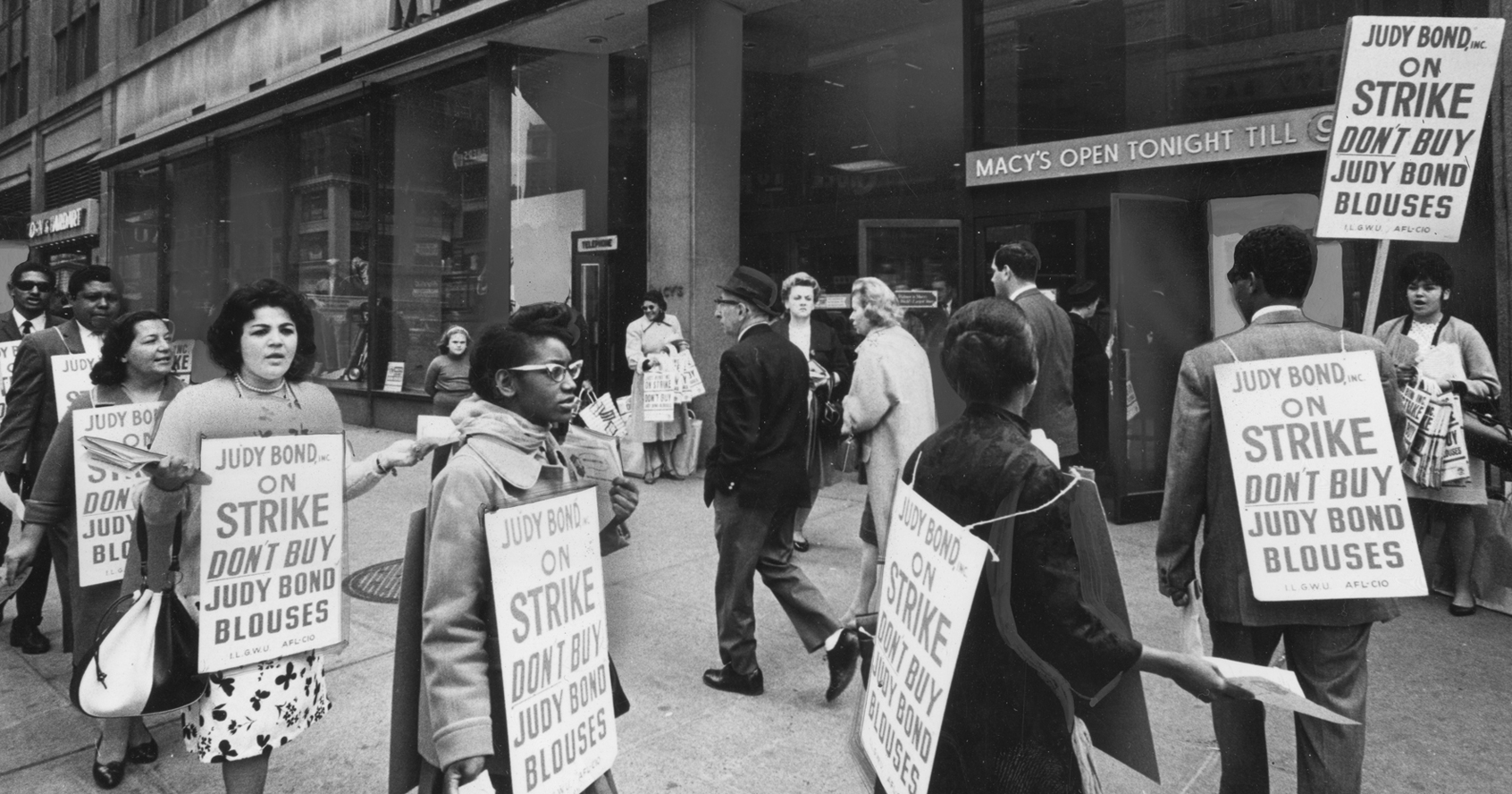 Um grupo de trabalhadores em greve marcham do lado de fora da Macy's enquanto usam cartazes incentivando as pessoas a não comprar blusas de Judy Bond