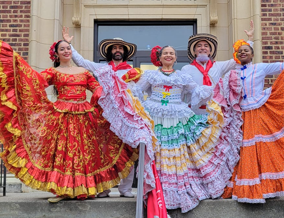 흐르는 듯한 밝은 옷을 입은 여성과 모자를 쓴 남성들이 포즈를 취하고 있다