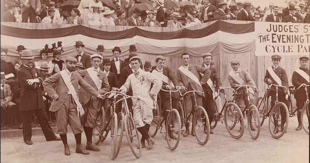 Os homens se alinham com suas bicicletas enquanto os espectadores observam de assentos elevados antes do The Evening Telegram Bicycle Parade