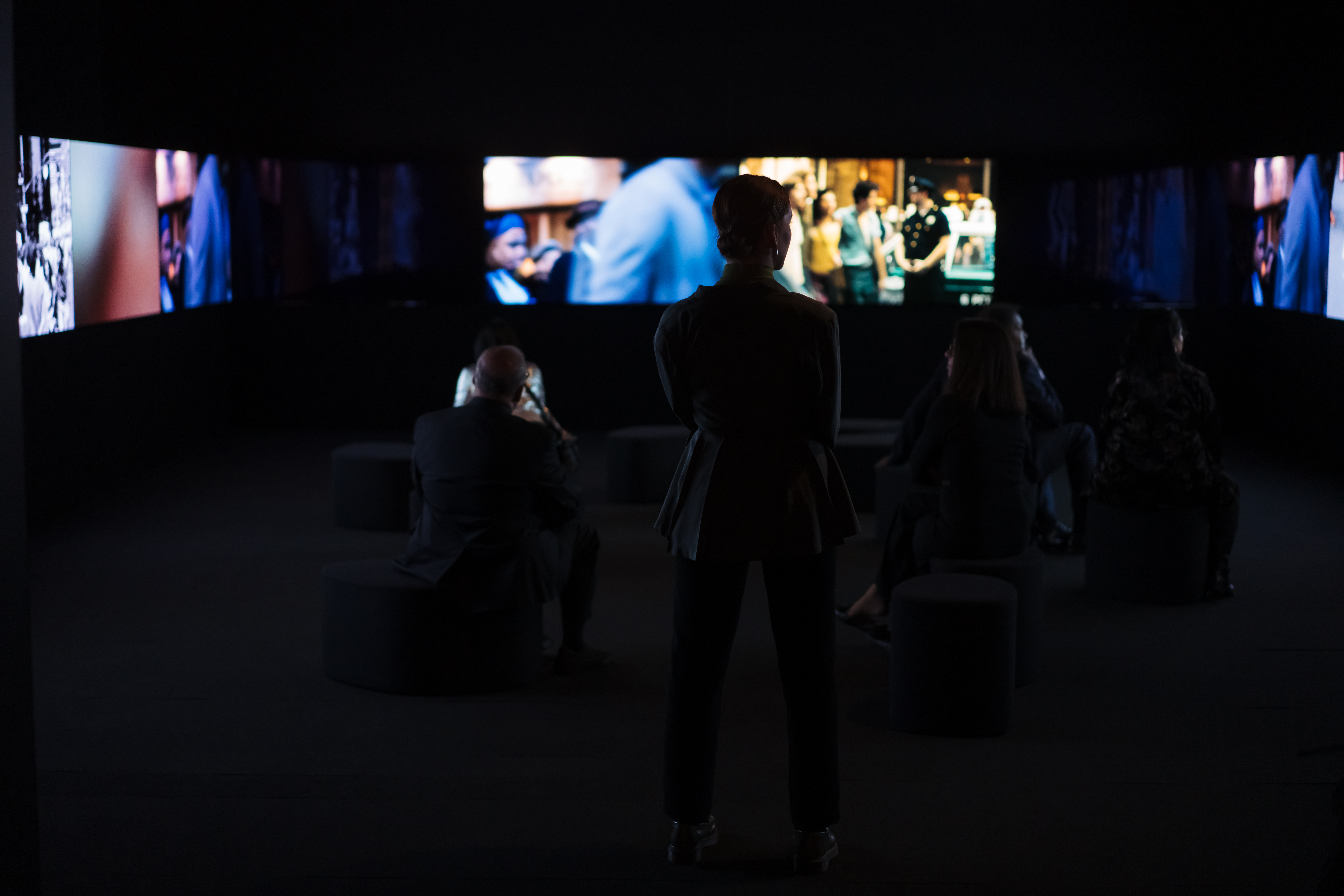 La silhouette d’une femme debout devant plusieurs écrans montrant des images floues de films.