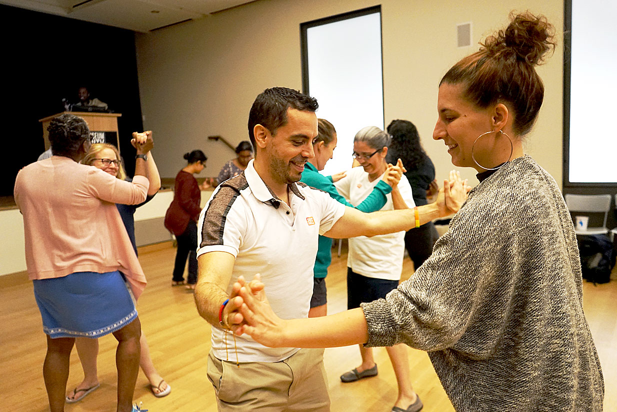 Educadores, de mãos dadas aos pares, participando de uma aula de dança de salsa durante o curso.