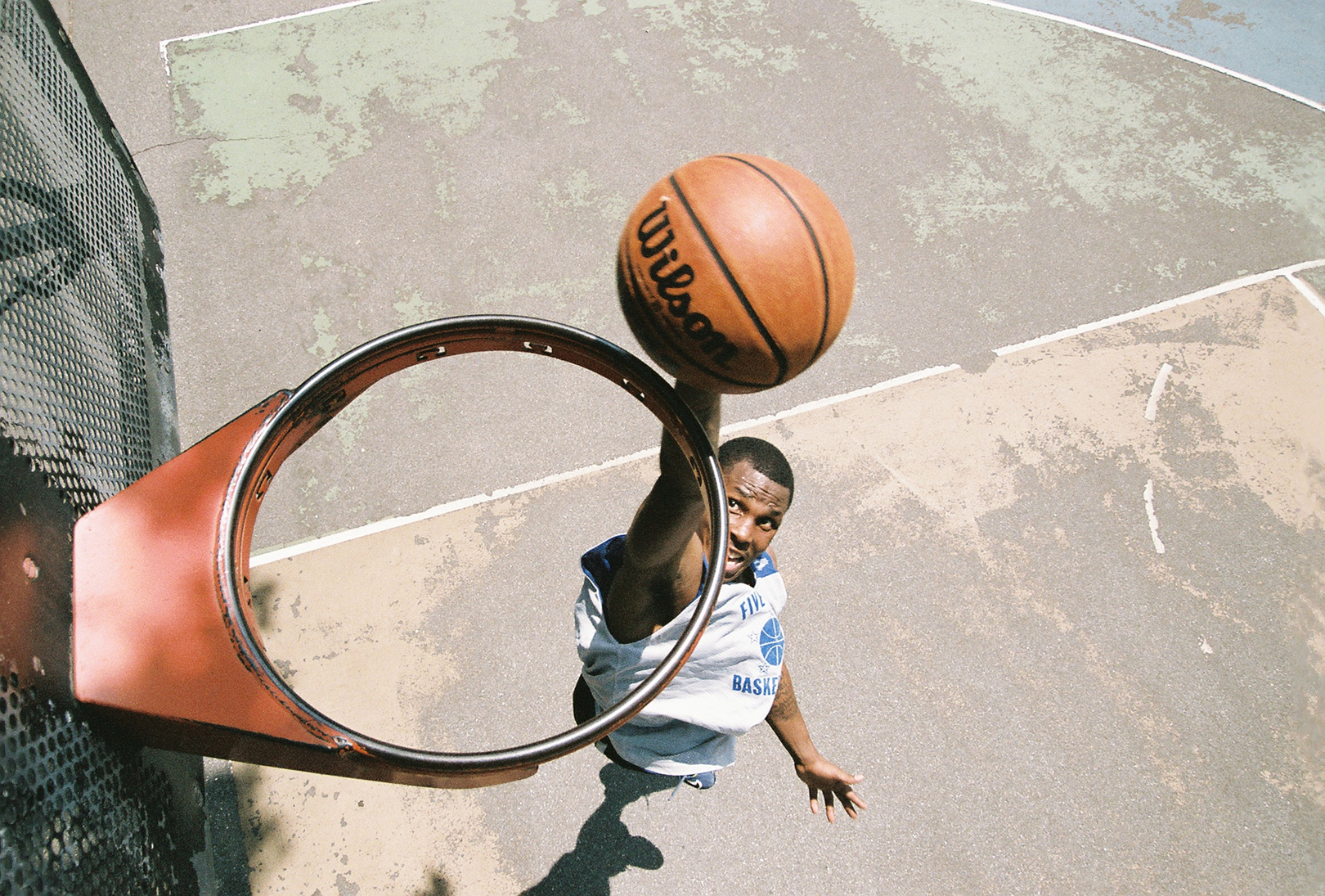 Vista de cima de uma cesta de basquete sem rede, onde um jogador é visto prestes a enterrar uma bola de basquete no aro