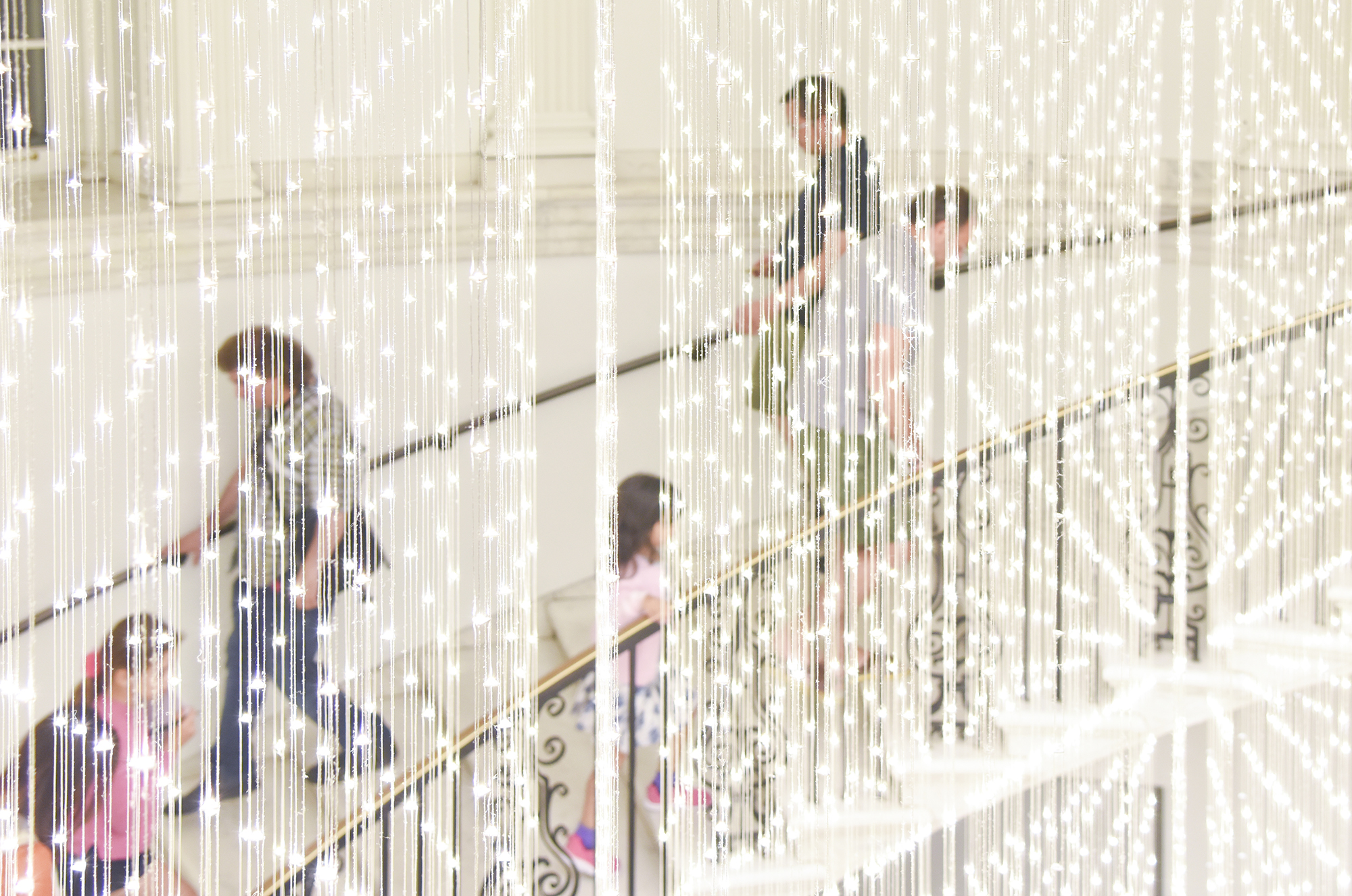 A crowd ascends a spiral staircase behind a light installation