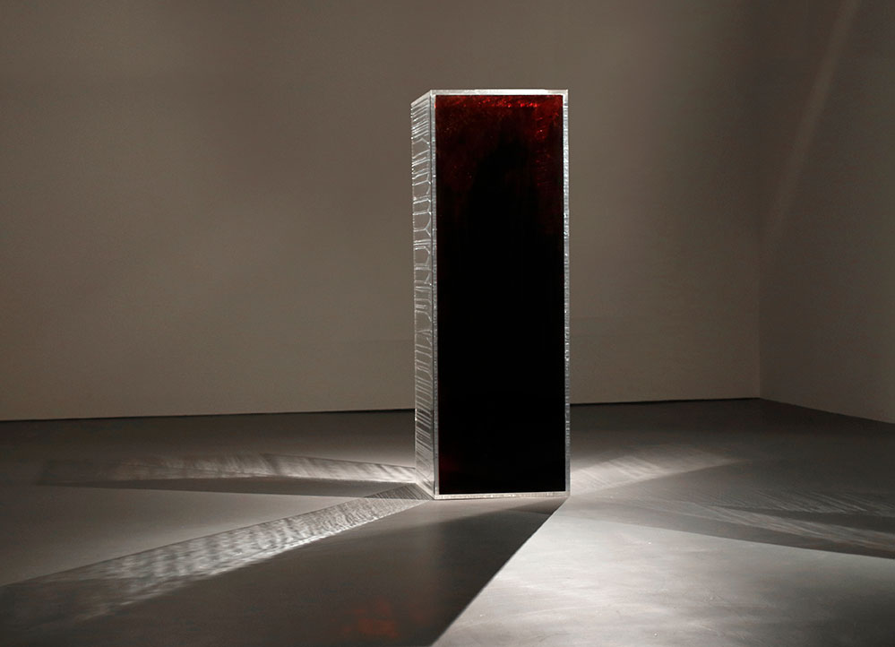 Rectangular prism that is reflective on two sides, and blood-red on the side facing the camera. Light is reflecting off it