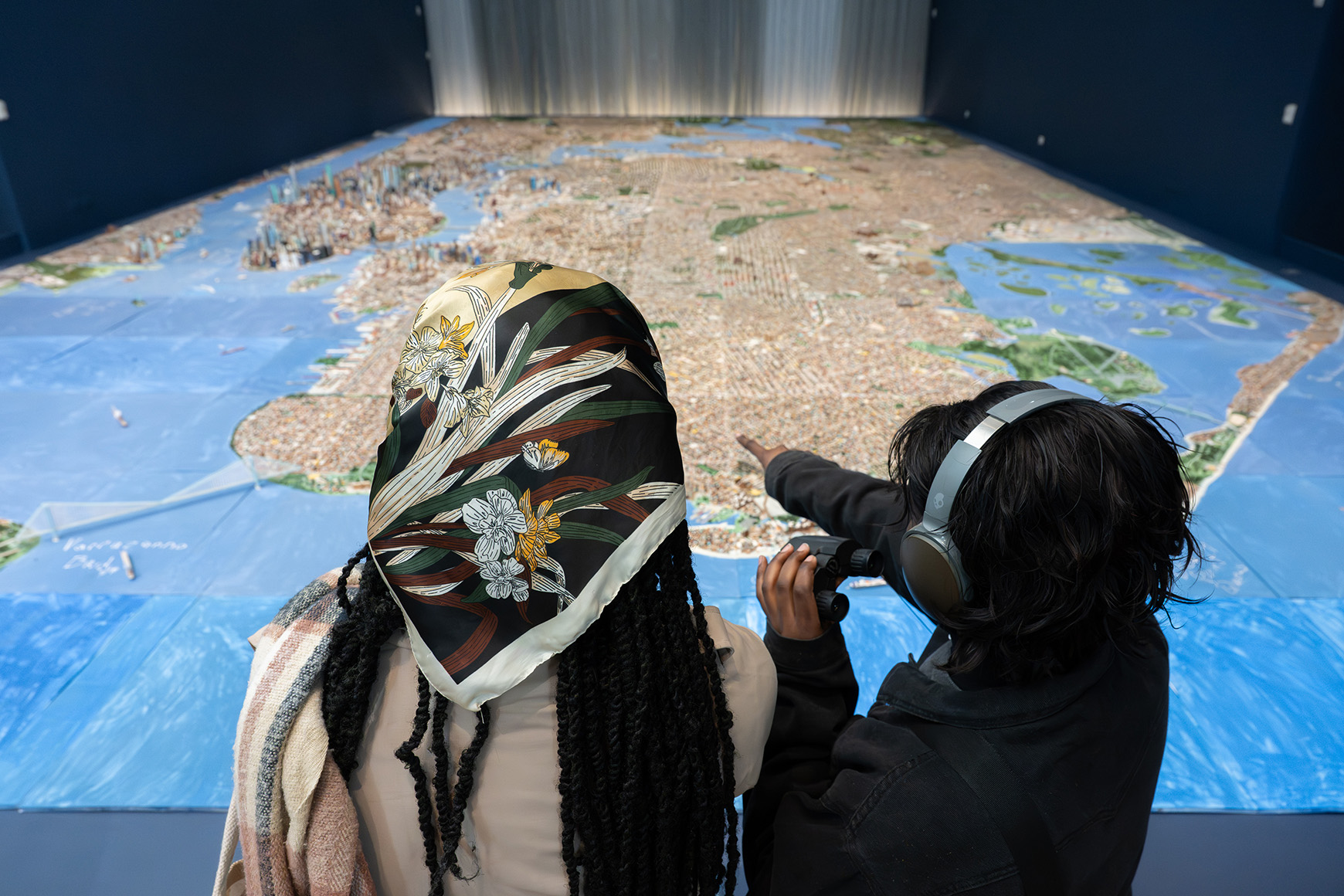 Two people looking and pointing at a handmade scale model of New York City
