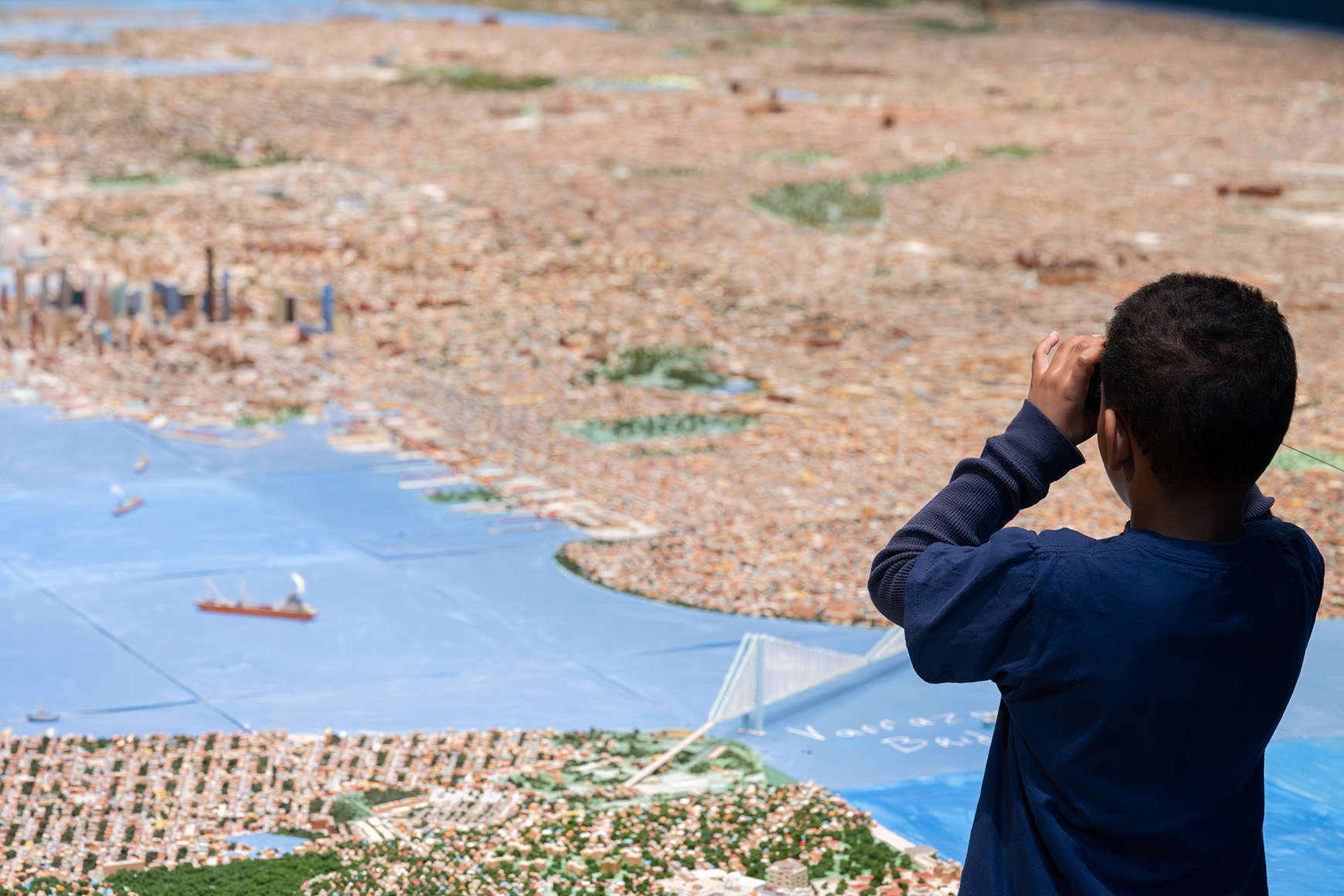 A child looking at a handmade scale model of New York City through binoculars
