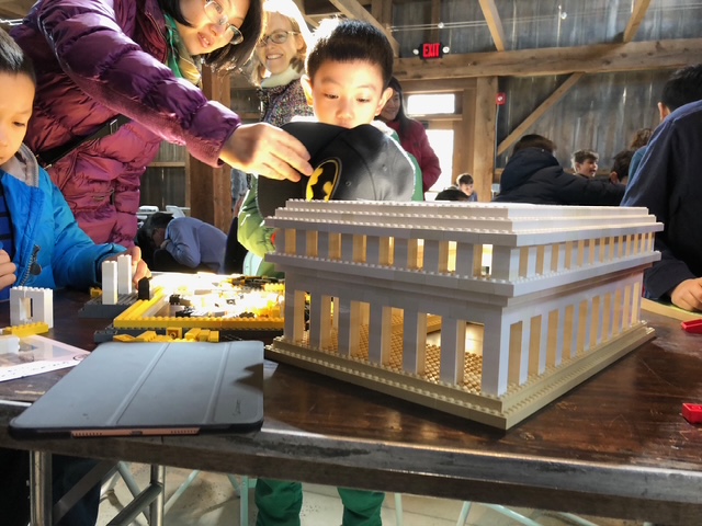 Picture of family of mother, boy, and child with an onlooker behind looking in awe at a LEGO construction