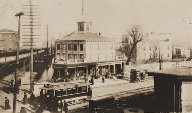 Photograph of an intersection with a trolly line on the street level, and elevated platform above.