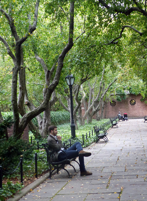 A man sits on a bench under the trees in the Conservatory Garden 