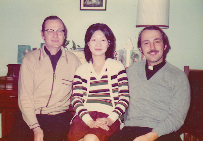 Color photograph of Fathers Denis Hanly (right) Joanna Chan, and Richard Grillo (left), sitting in a living room.