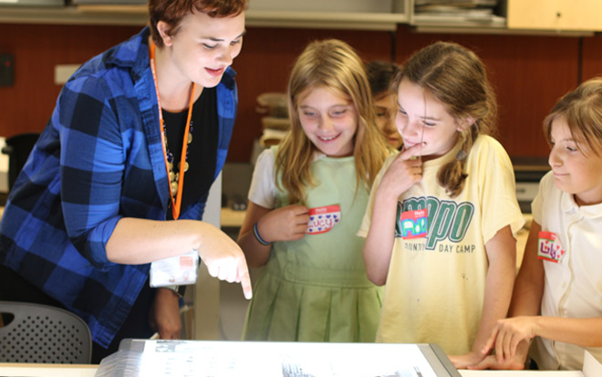 Three kids look at a photograph on a lightbox with a museum photography instructor 