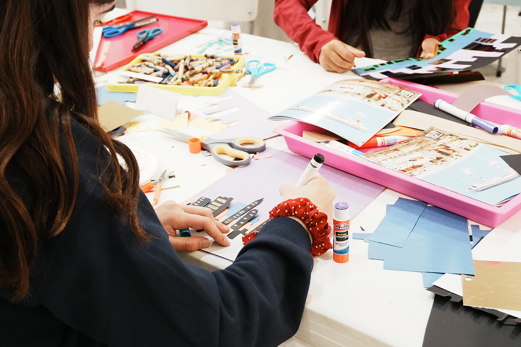 Two children creating an artwork with glue and cut paper.
