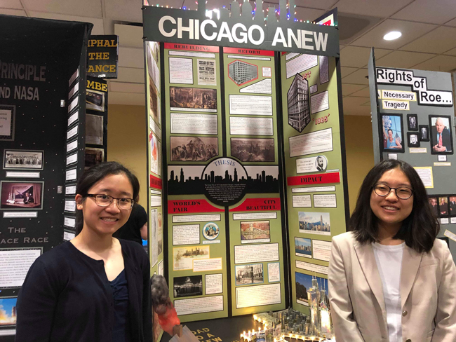 Dos estudiantes se paran a ambos lados de su proyecto del Día de la Historia, un panel de exhibición que se centró en "La tragedia del gran incendio y el triunfo de la ciudad de los rascacielos"