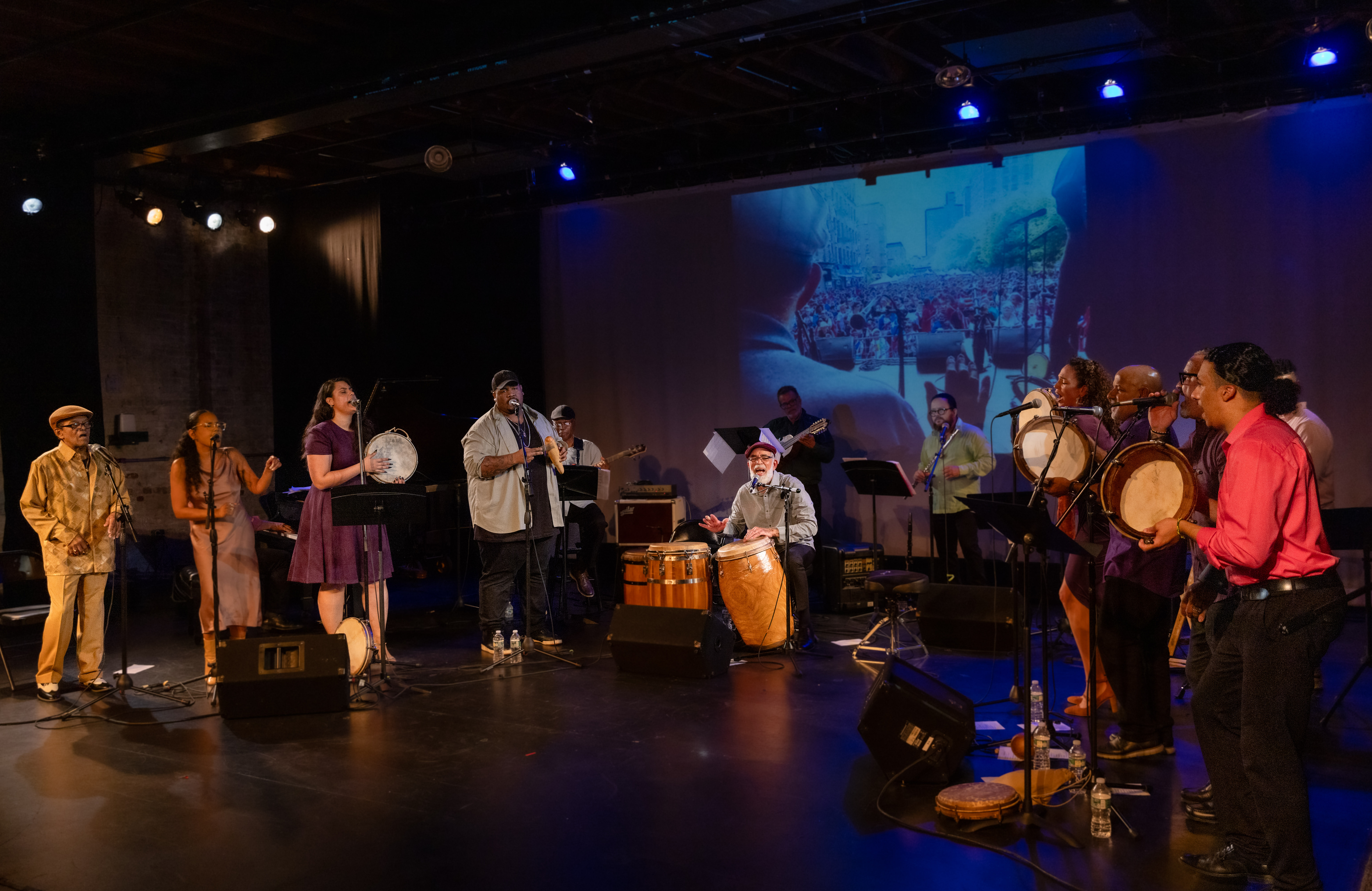 A group of people perform and play drums on a stage. 
