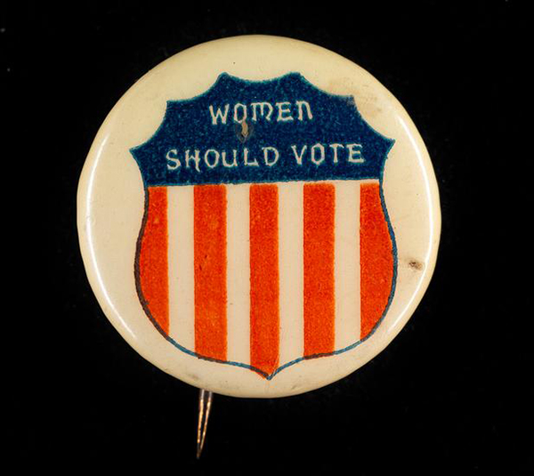 Women’s Suffrage button that says “Women Should Vote” with an image of shield with the red, white, and blue coloring of the American flag. 