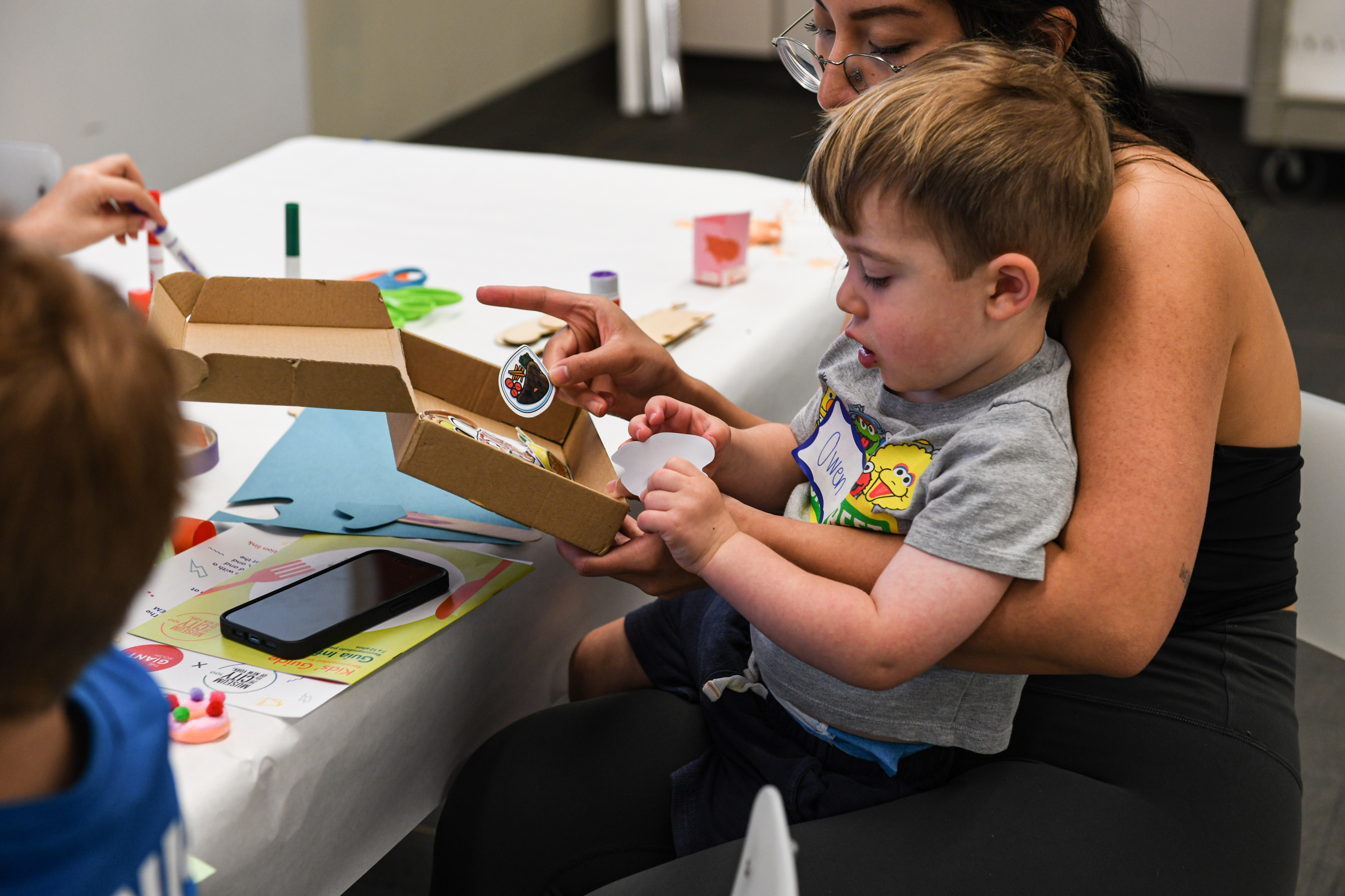 A woman holds a toddler as they make art.