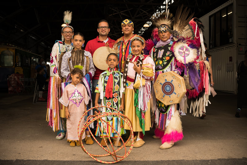 Um grupo de adultos e crianças em trajes tradicionais posam para uma fotografia de grupo.
