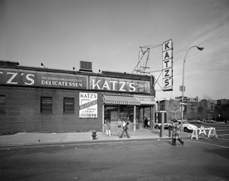 Vista exterior de Katz's Delicatessen en la intersección de las calles Ludlow y Houston con algunas personas caminando.