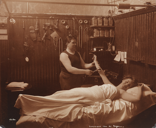 A woman reposing, receiving some sort of massage therapy in a Turkish bath.