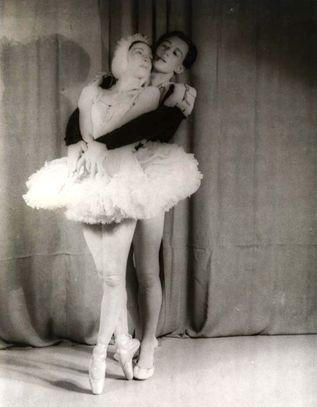 Two ballerinas, a man and a woman in costume, pose in together.