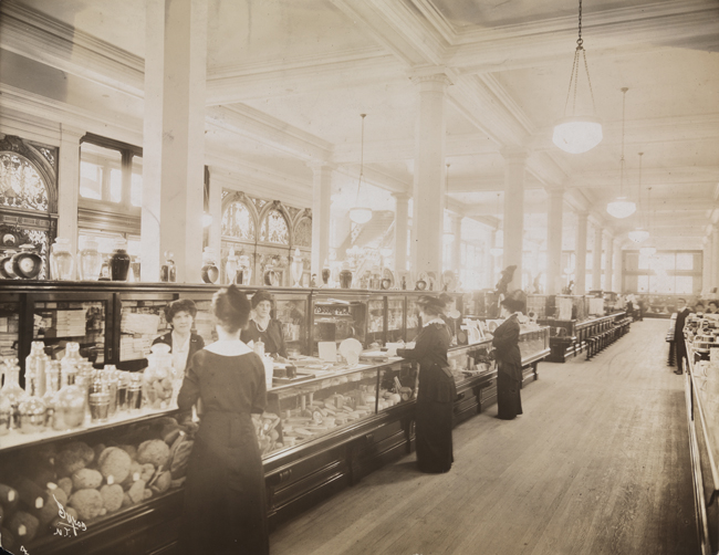 Women sales clerks and customers at a cosmetics counter in a dry goods store.