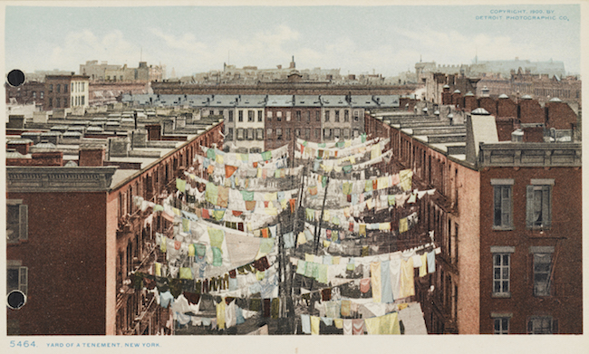 A color postcards showing rows of clotheslines with laundry hanging off them between two rows of apartment buildings.