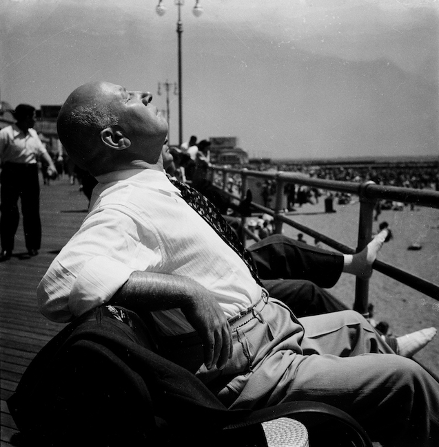 Black and white photo of a man relaxing on a bench on the boardwalk