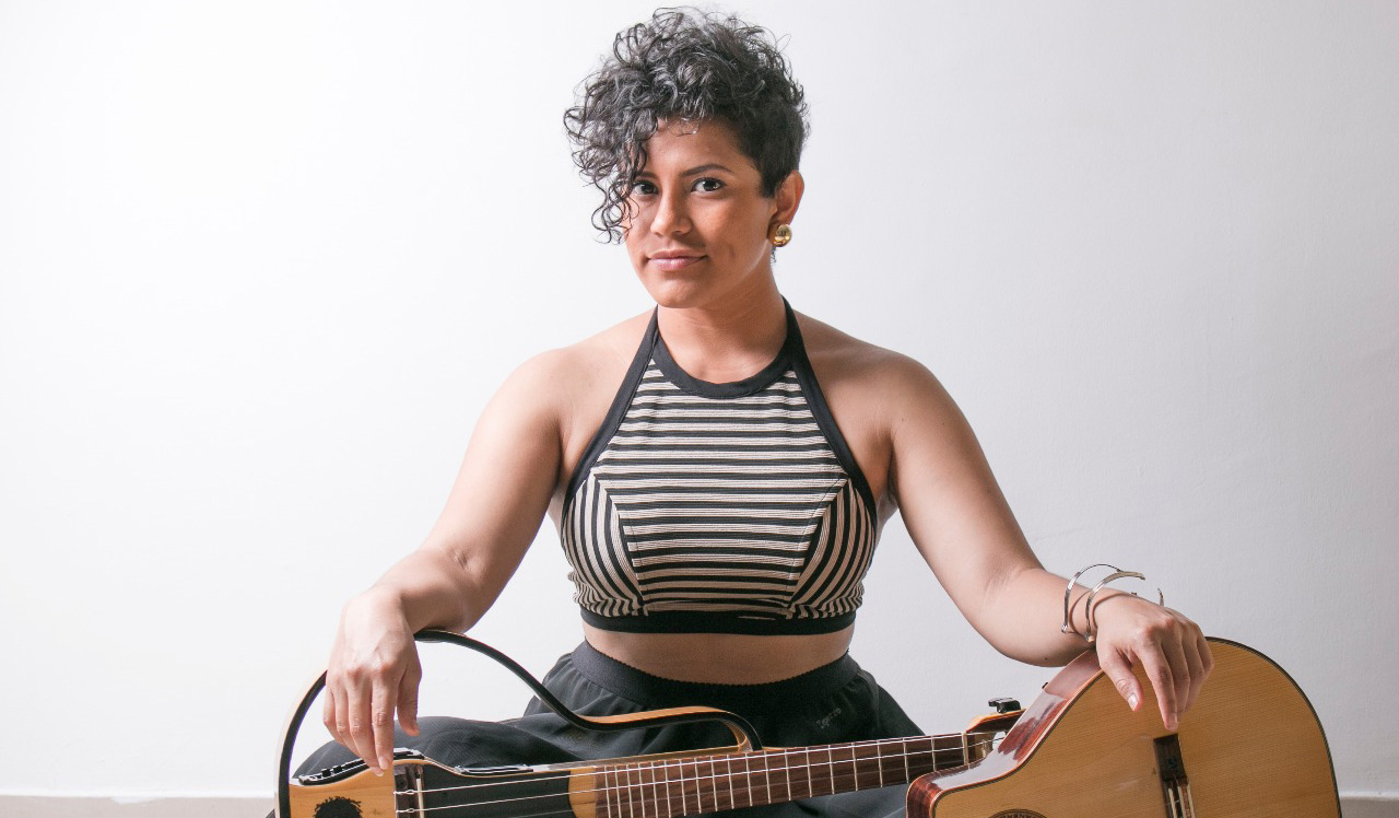 A woman sits with two guitars against a white backdrop.