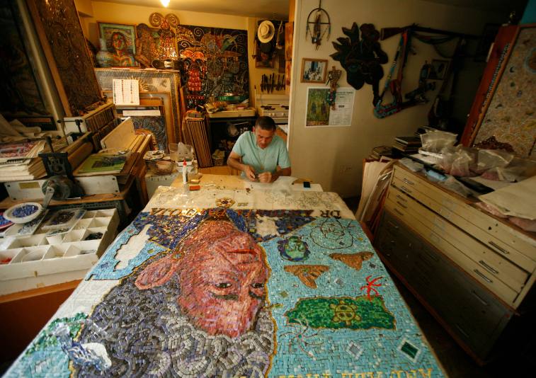 Manny trabalha em um enorme mosaico em andamento sobre uma mesa em seu estúdio caseiro.
