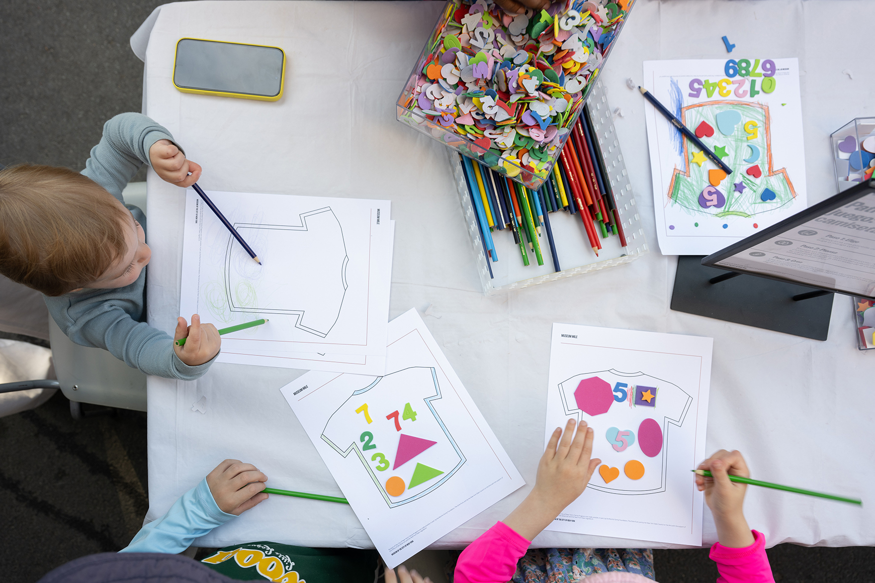 Three children creating an artwork with colored pencils and cut paper.