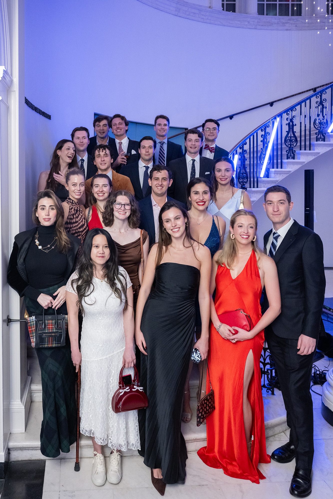 A group in cocktail attire stands on a spiral marble staircase