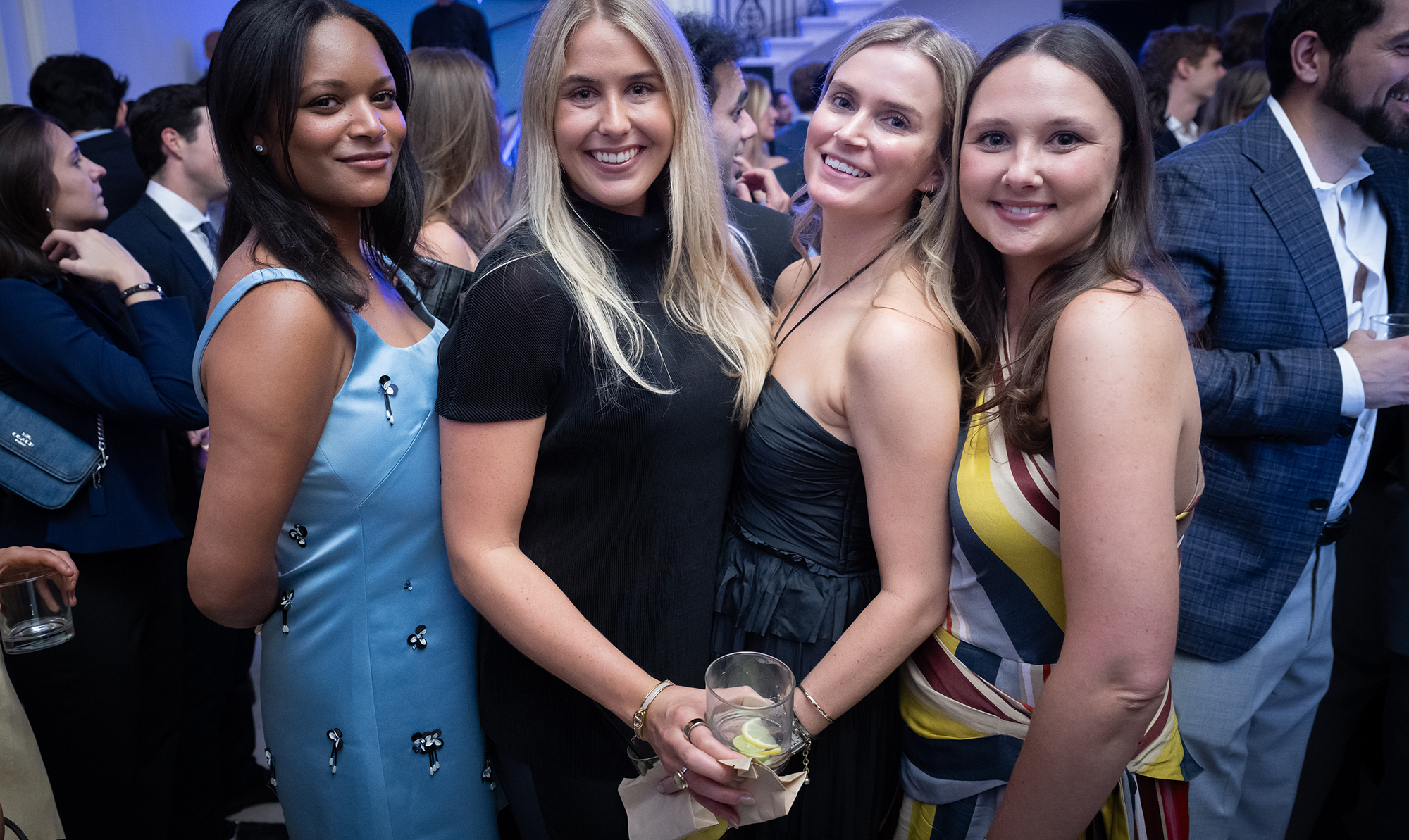 Four people in cocktail attire pose within a crowd