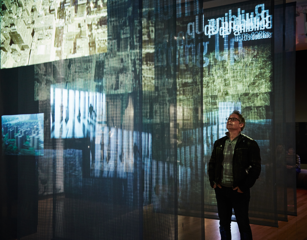 A visitor stands in-between sheer panels as a video projection plays across them