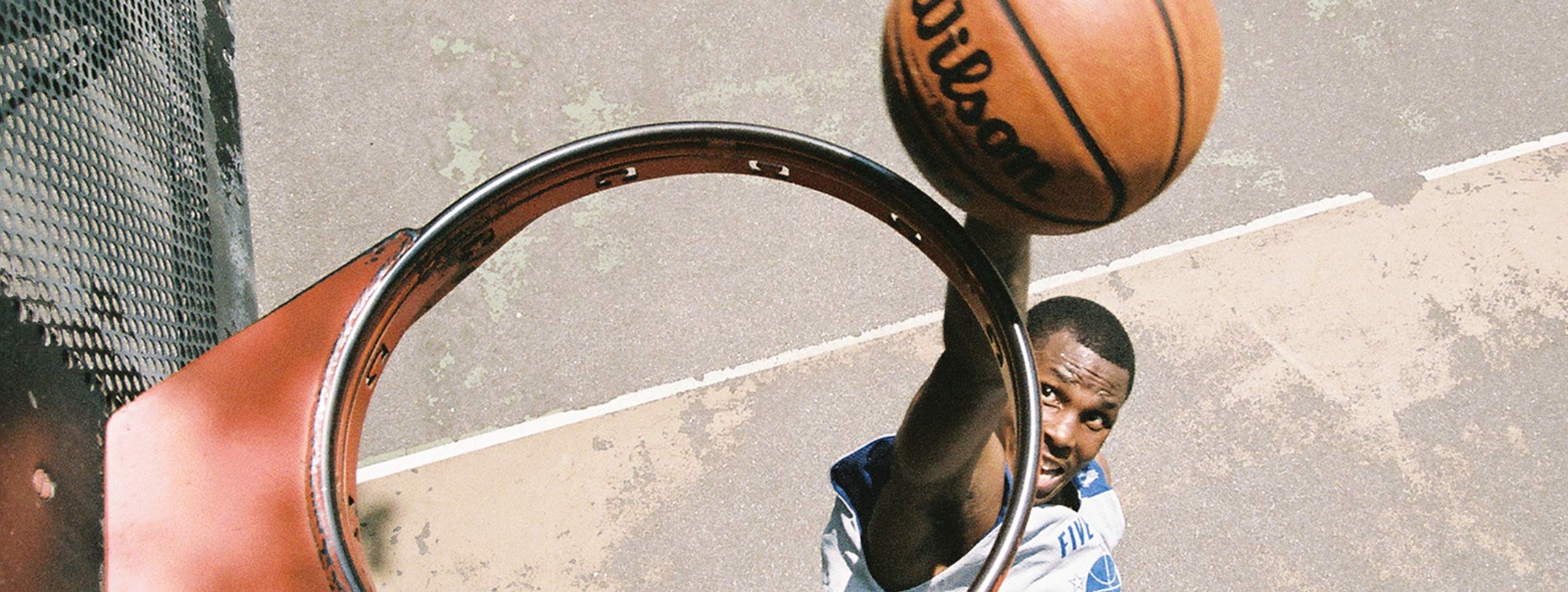 Vue de dessus d'un panier de basket sans filet, où un joueur est vu sur le point de plonger un ballon de basket à travers le panier