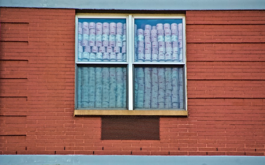 Two windows in an brick building that are filled with stacks of toilet paper rolls.