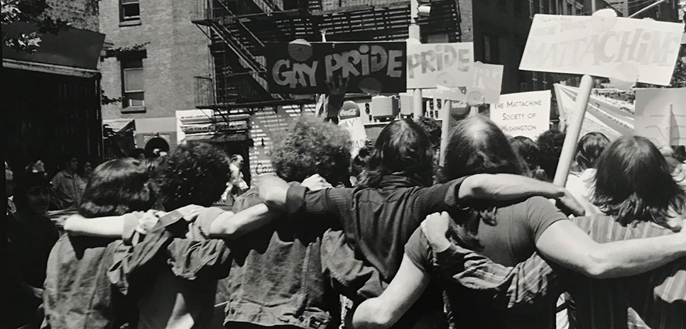 Photograph by Fred W. McDarrah of a group of people with their arms around each other and holding signs related to Pride