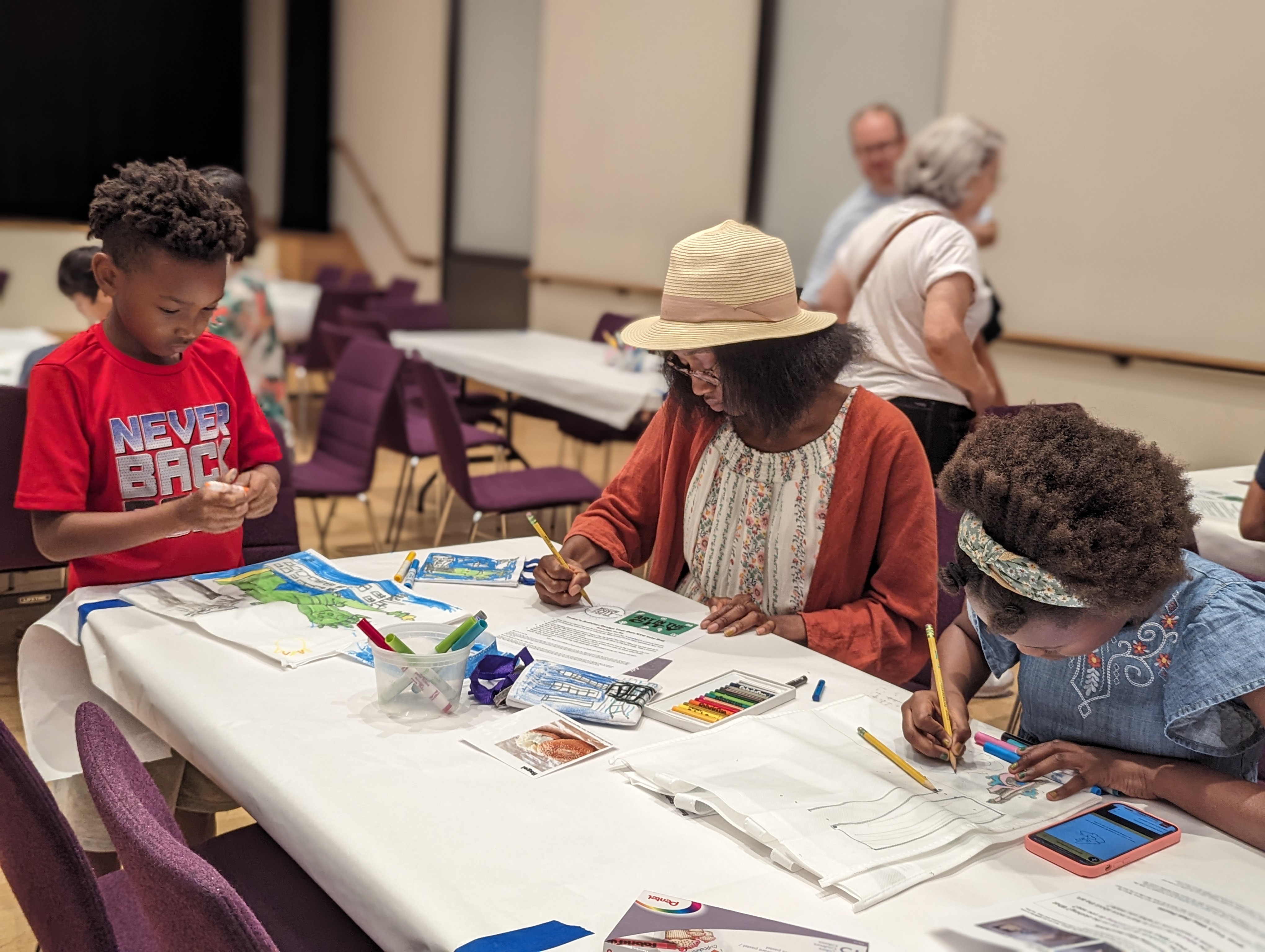 Three people draw at a table. 