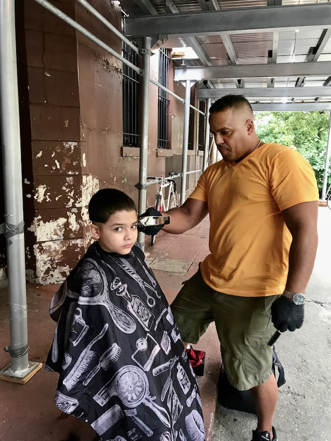 A man gives a young boy a haircut outdoors.