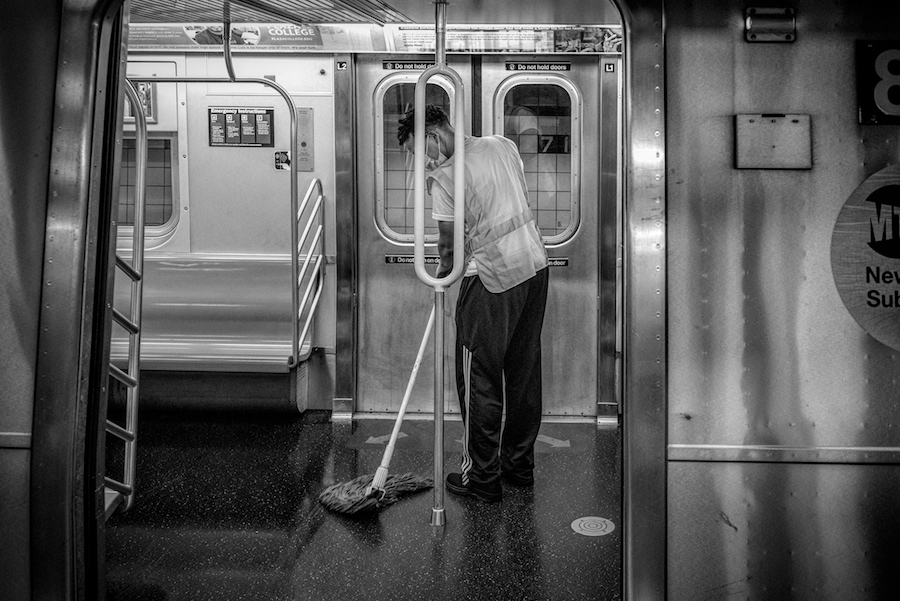 A man with a mop cleans the floor of a subway car in front of a subway door.