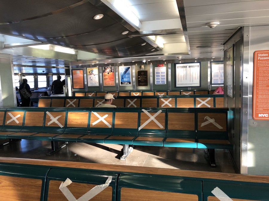 A photograph of the Staten Island Ferry, with "X's" taped over every other seat on the benches.
