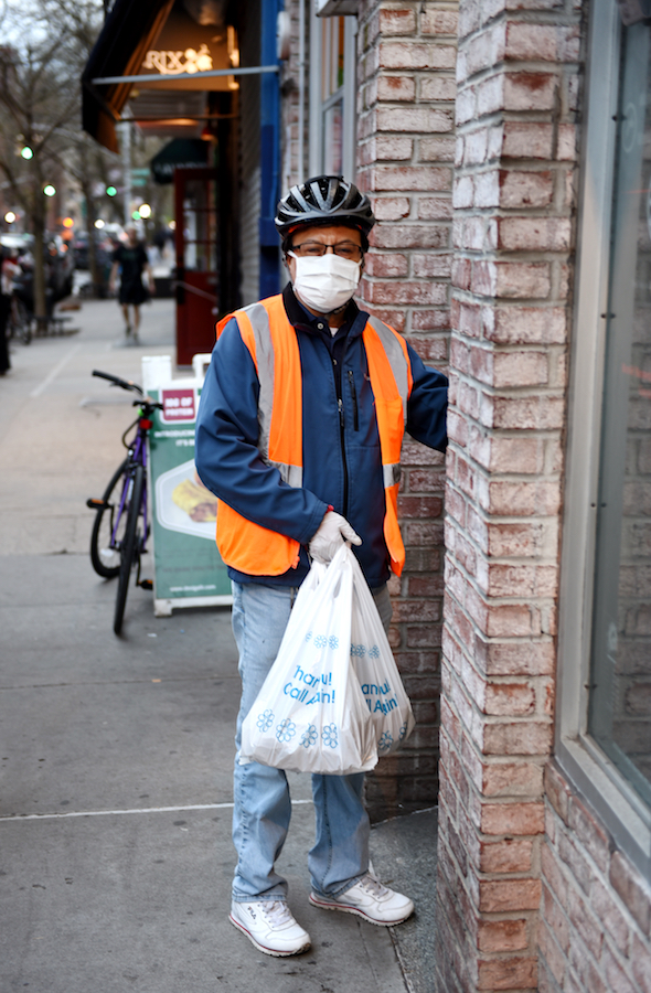 A delivery worker in a mask stands outside of a building.