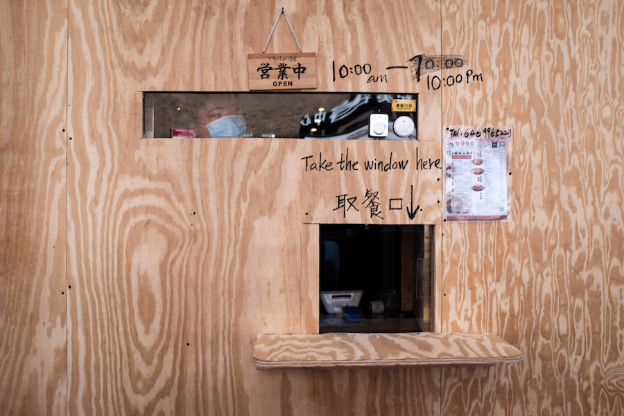 Plywood in front of a restaurant window, with small openings for take out and taking orders.