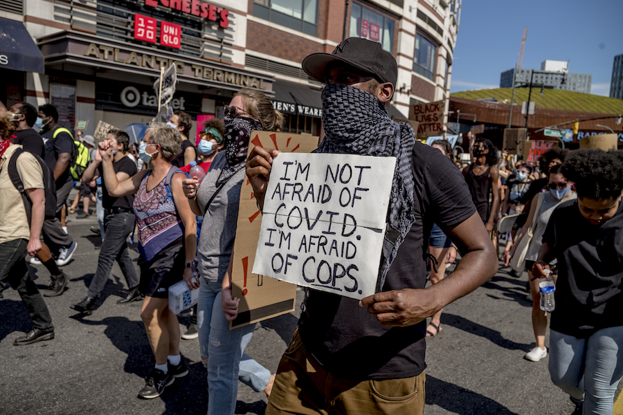 une foule de manifestants portant des masques et tenant des pancartes. On lit: "Je n'ai pas peur du COVID - j'ai peur des flics."
