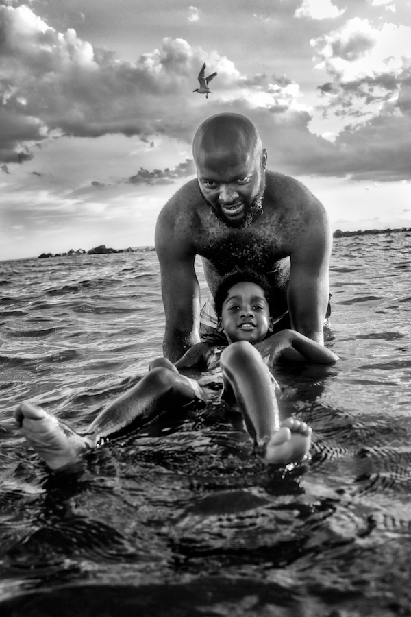 A man stands in the water, holding a young child