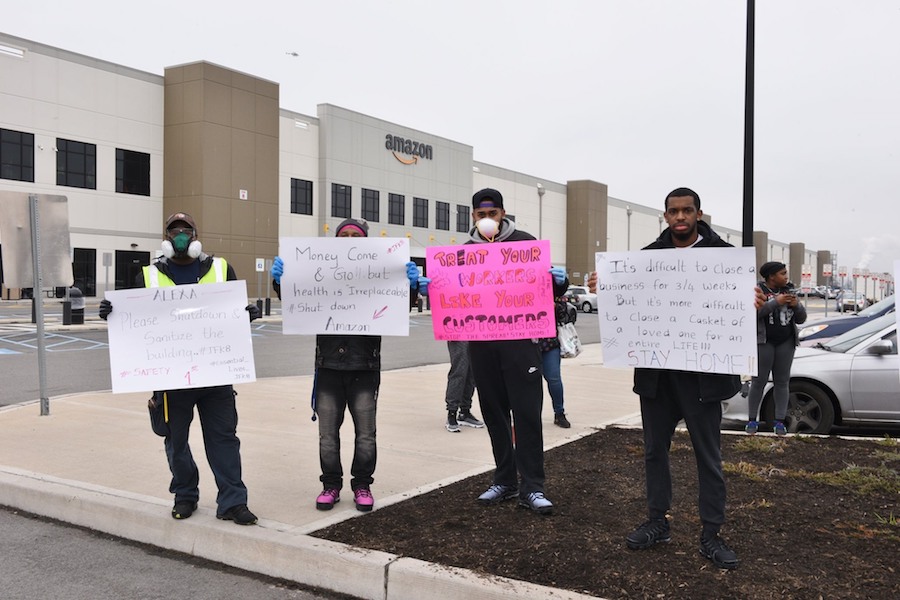 Quatre travailleurs d'Amazon protestent pour la sécurité avec des messages sur des panneaux fabriqués par eux-mêmes devant un entrepôt Amazon.