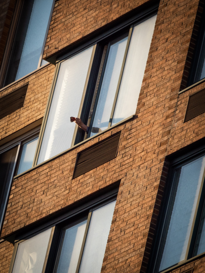 Someone holds a clapper outside an apartment window as part of the "7pm salute" during the COVID-19 pandemic.